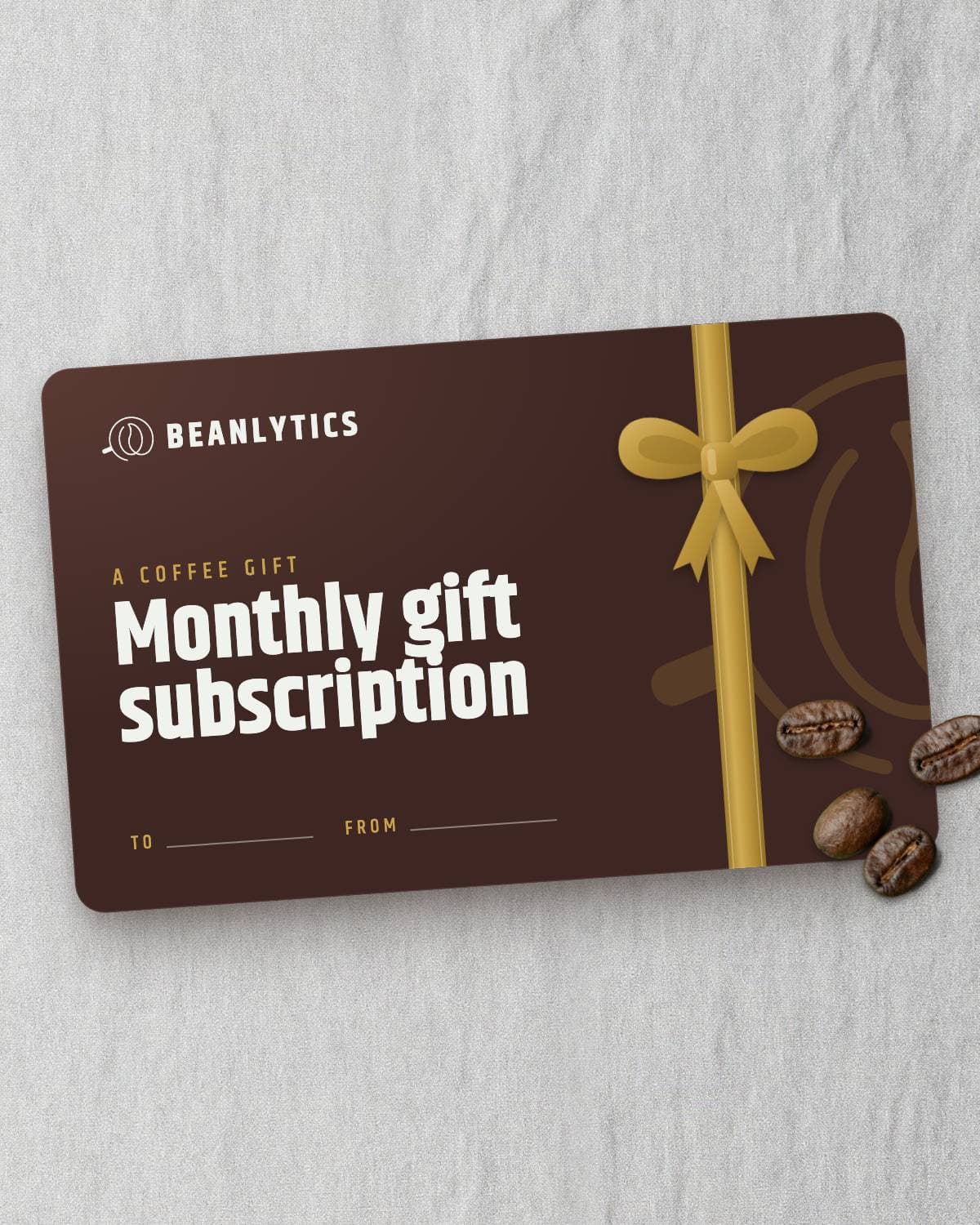 Monthly gift subscription card printed with a gold ribbon and bow, coffee beans resting on its corner