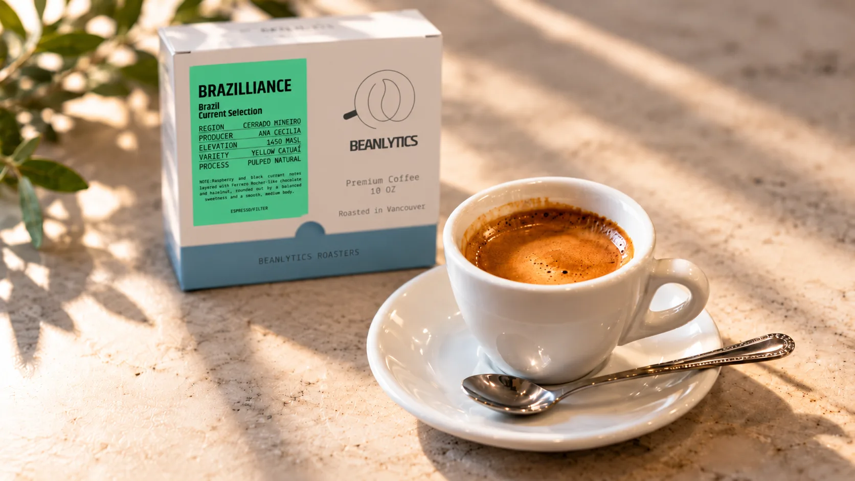 An espresso in a white cup and saucer beside a box of Beanlytics Brazilliance, a pulped natural Yellow Catuai from Cerrado Mineiro, Brazil, on a sunlit stone counter.